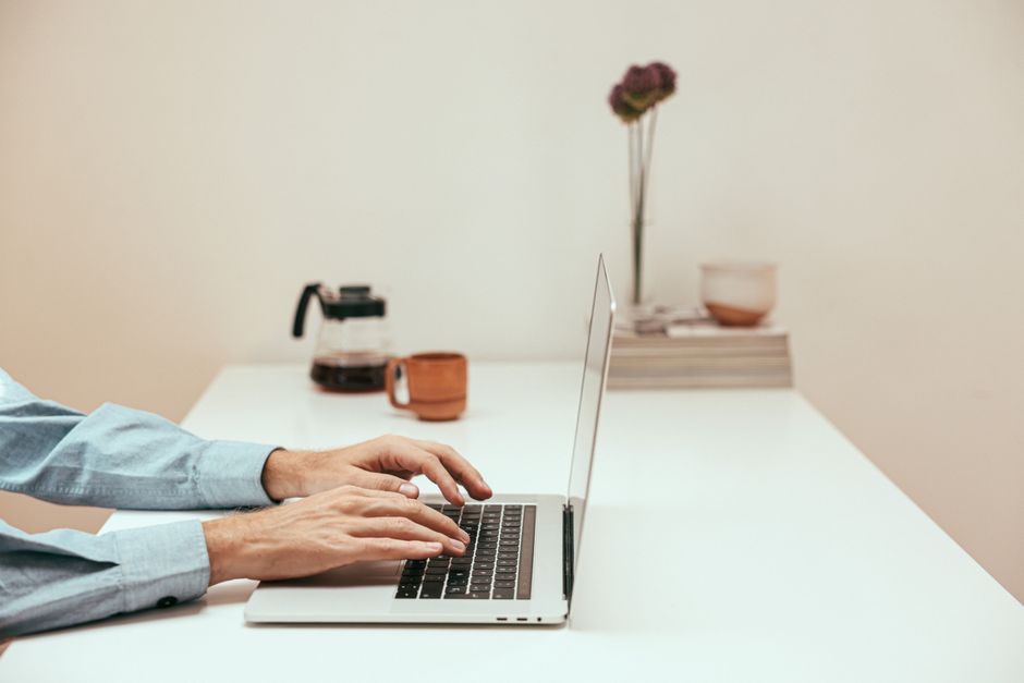 Manos escribiendo en una laptop en una oficina moderna, representando el trabajo remoto de seguimiento de proyectos
