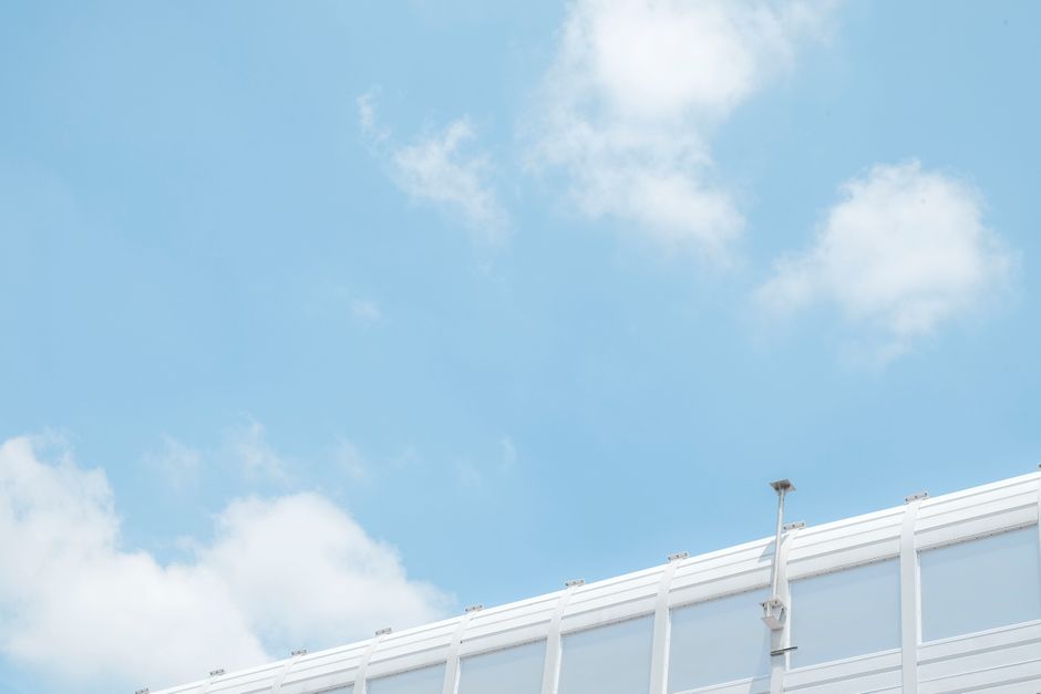 Imagen minimalista de una cámara de seguridad contra un cielo azul brillante con nubes dispersas