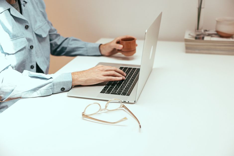 Espacio de trabajo informal con laptop, taza de café y anteojos sobre una mesa blanca.