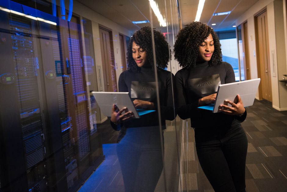 Mujer afroamericana de pie en una oficina moderna usando un portátil, reflejando profesionalismo y compromiso tecnológico